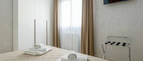 A hotel room with a bed, a TV mounted on the wall, and a towel rack.