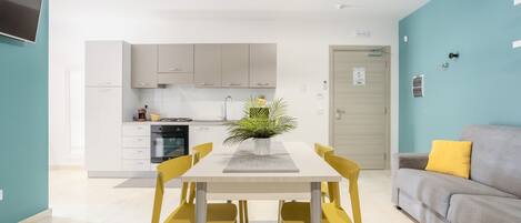 A modern kitchen with white cabinets, a dining table with yellow chairs, and a grey sofa with a yellow pillow.