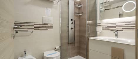 A modern bathroom with a glass-enclosed shower, a bidet, a toilet, and a vanity with a mirror.