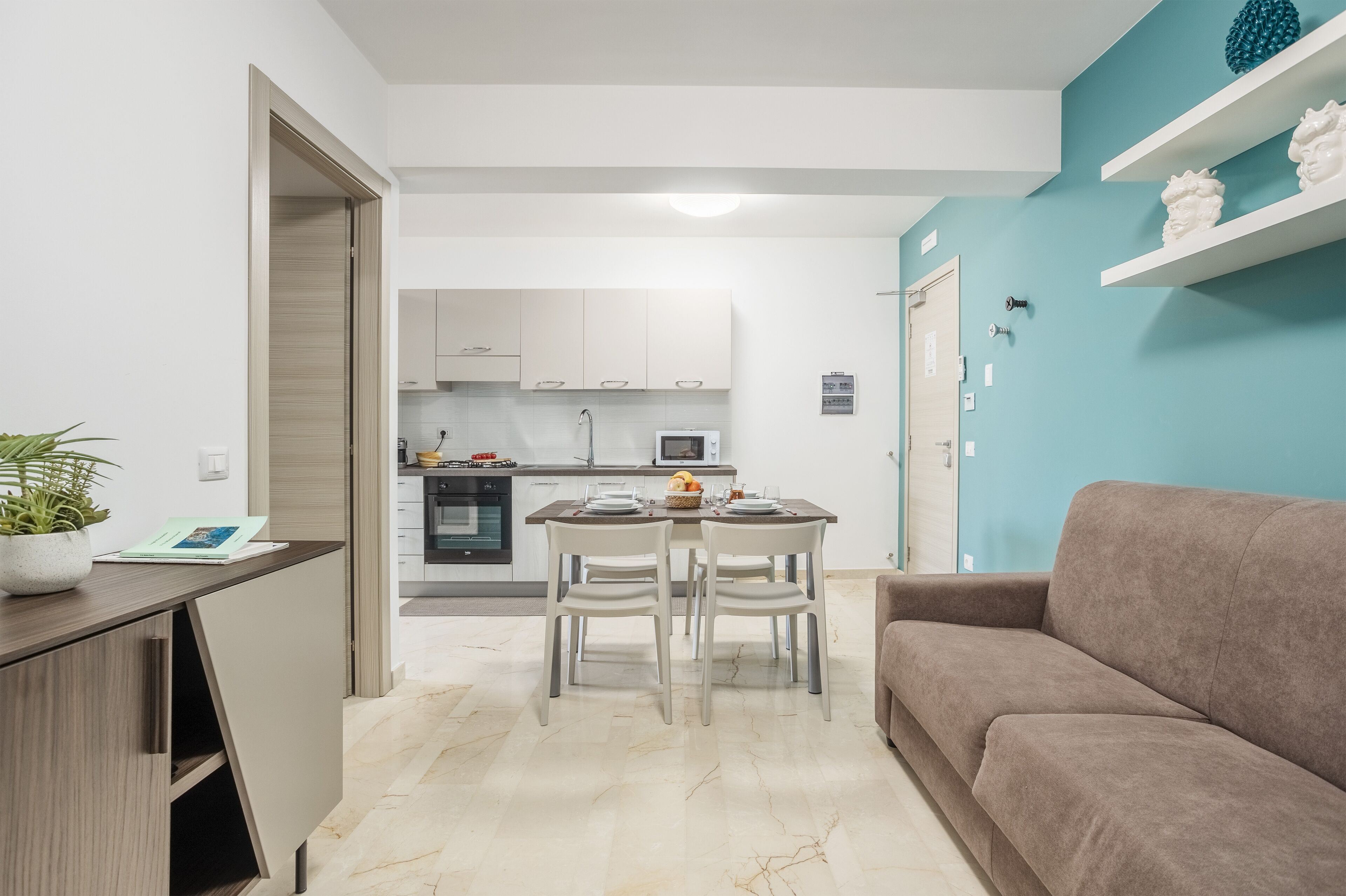 Una cucina moderna con mobili bianchi, un tavolo da pranzo con sedie e una parete blu a contrasto.