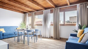 A modern living room with a wooden ceiling, a blue sofa, a dining table with chairs, and large windows with curtains. - Azzurra Apartments (Balestrate)