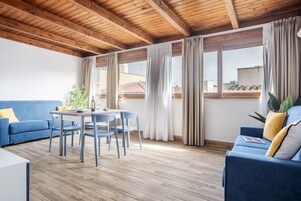 Una sala de estar moderna con techo de madera, un sofá azul, una mesa de comedor con sillas y ventanas grandes con cortinas.
