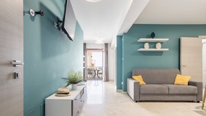 A modern living room with a grey sofa, a small white side table, and a teal accent wall. - Azzurra Apartments (Balestrate)