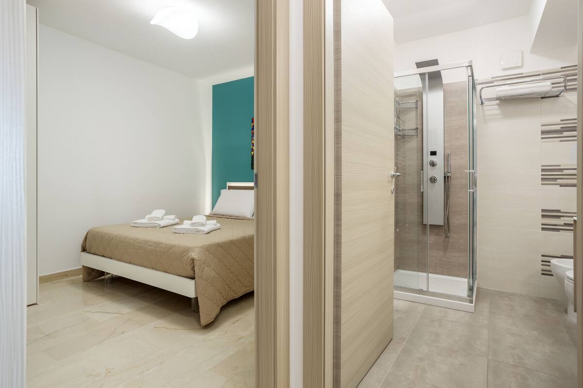 A modern bedroom with a bed, a glass shower enclosure, and a bathroom with a toilet and sink.