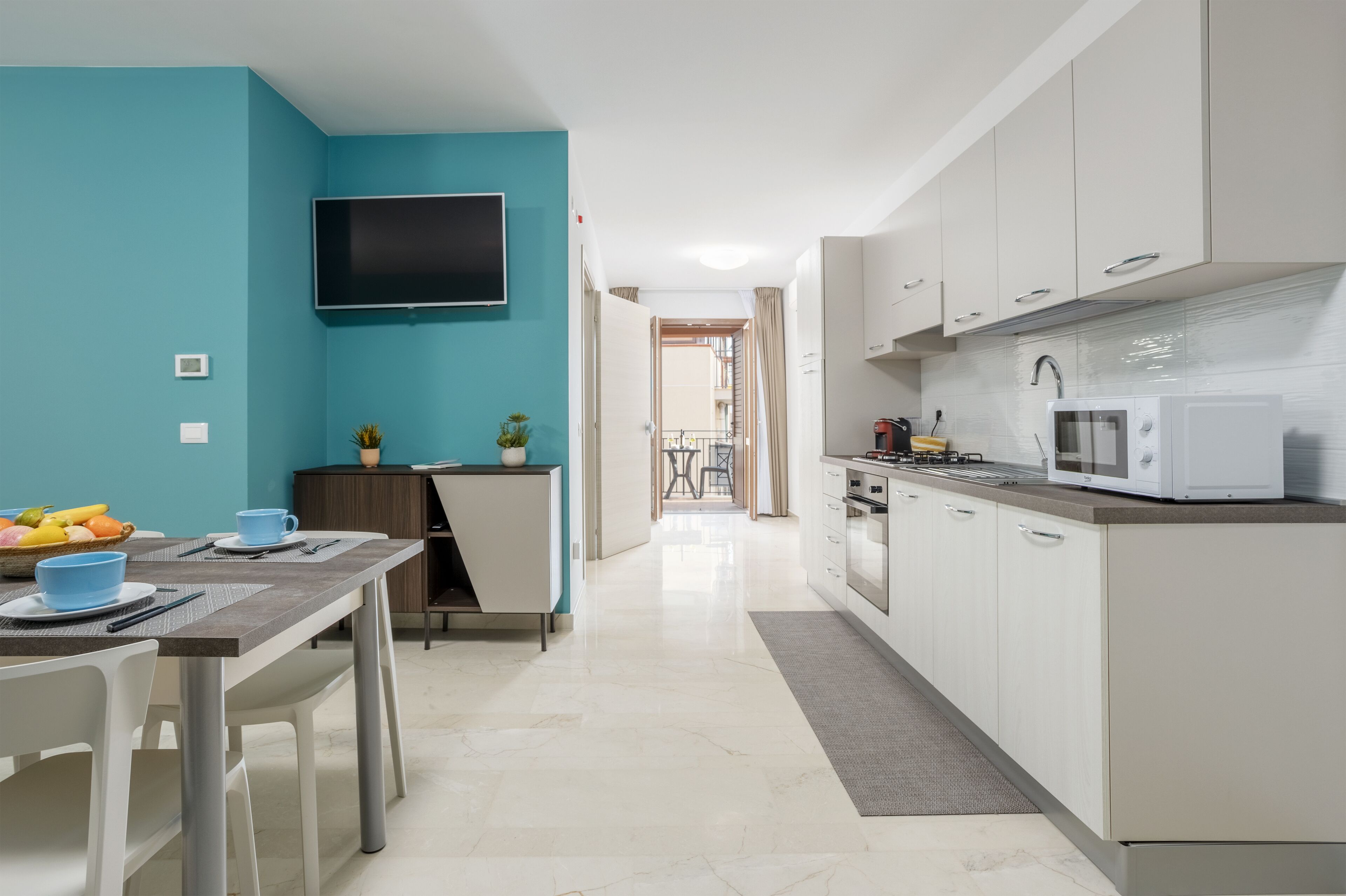 A modern kitchen with white cabinets, a flat-screen TV, and a dining area with a table and chairs.