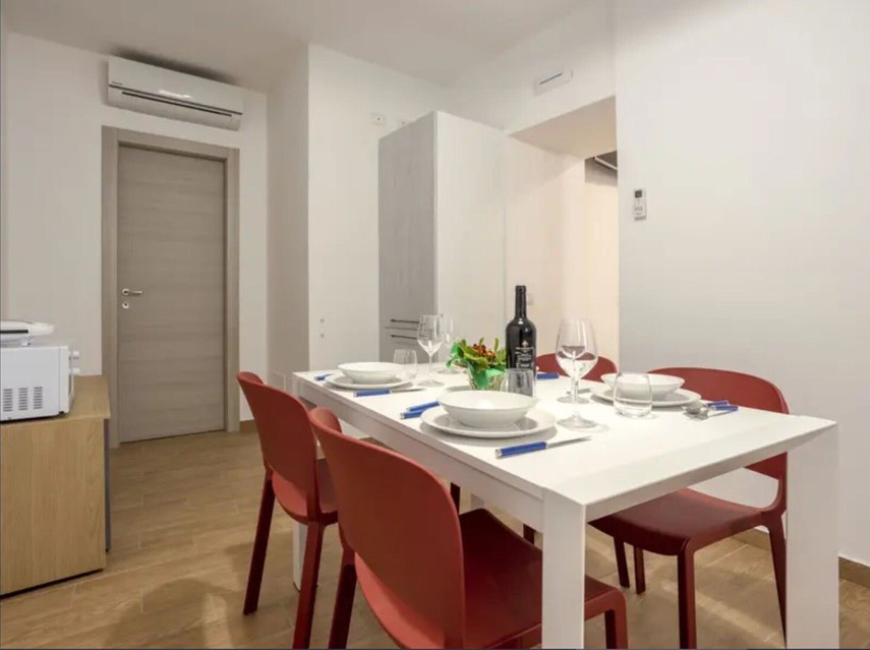 A dining area with a white table set for four, red chairs, a bottle of wine, and a small plant on the table.
