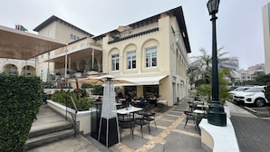Ein Straßencafé mit Tischen und Stühlen, einem dekorativen Lampenpfosten und einem Gebäude mit Balkon.