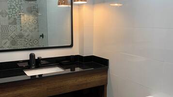 A modern bathroom with a glass shower enclosure, a wooden vanity with a black countertop, a white toilet, and pendant lighting.