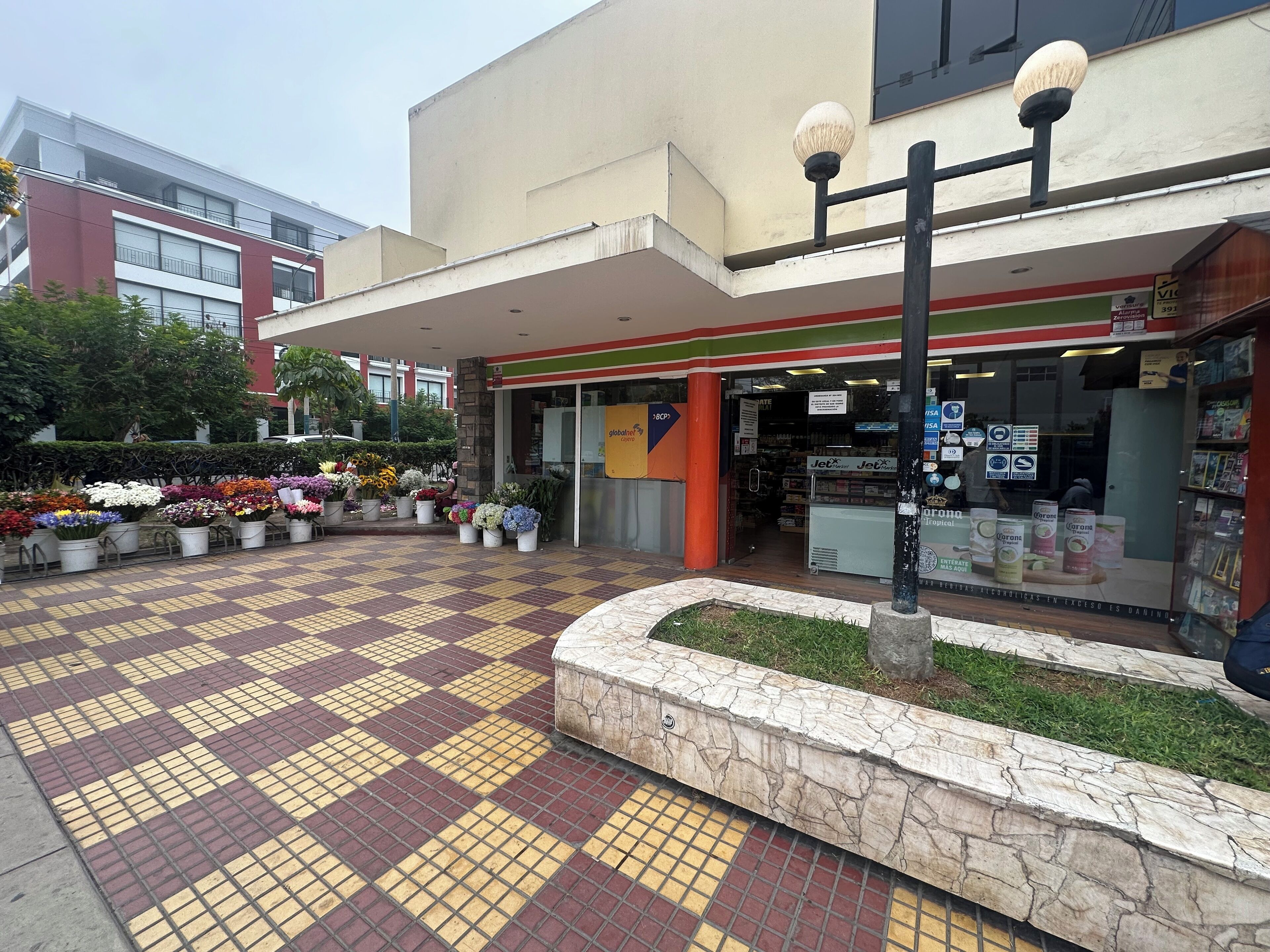 Un edificio con un área de entrada empavedada, una floristería y una tienda visible con varios carteles.