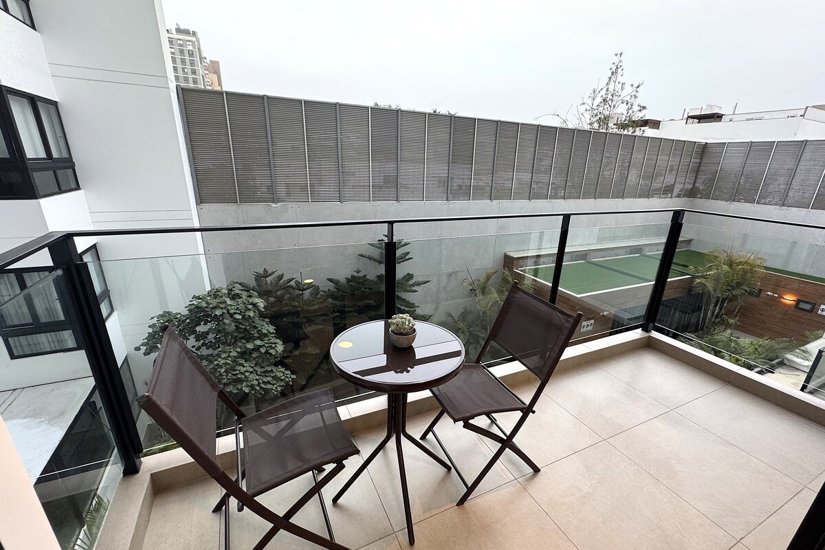 A balcony with a glass railing, two chairs, a small round table, and potted plants.