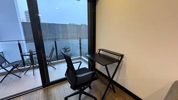 A modern room with a glass door leading to a balcony, a black office chair, a small round table, and a black desk.