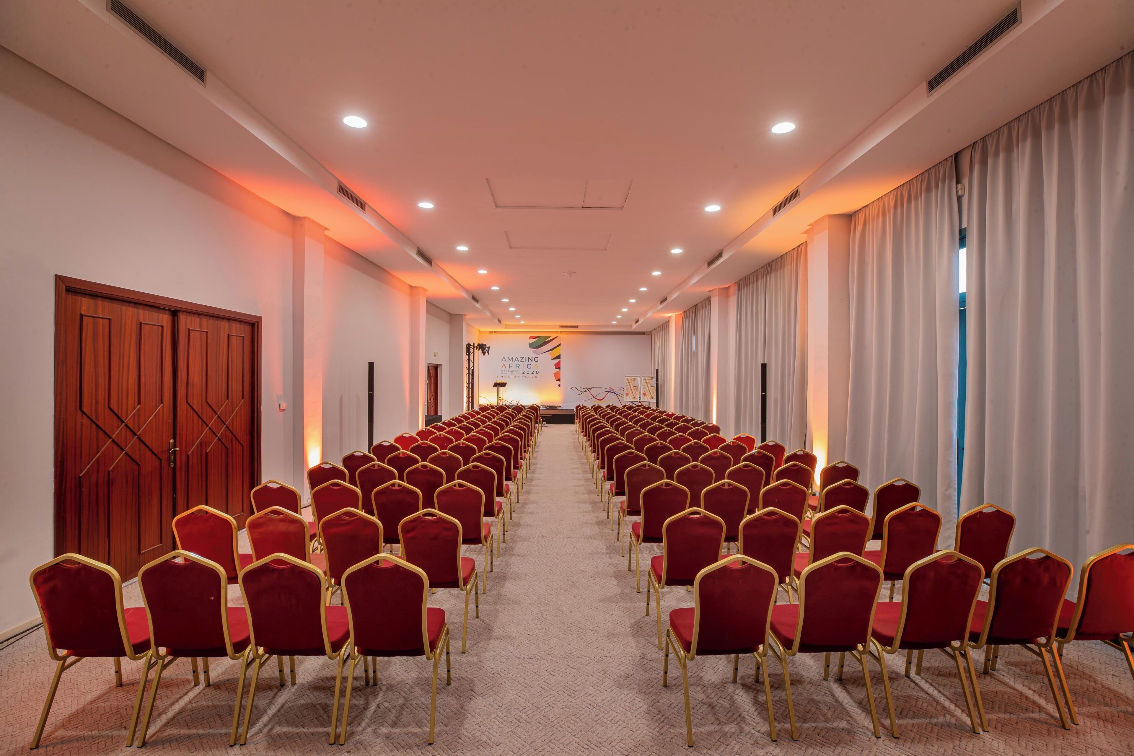 A conference room with rows of red chairs and a wooden door on the left.