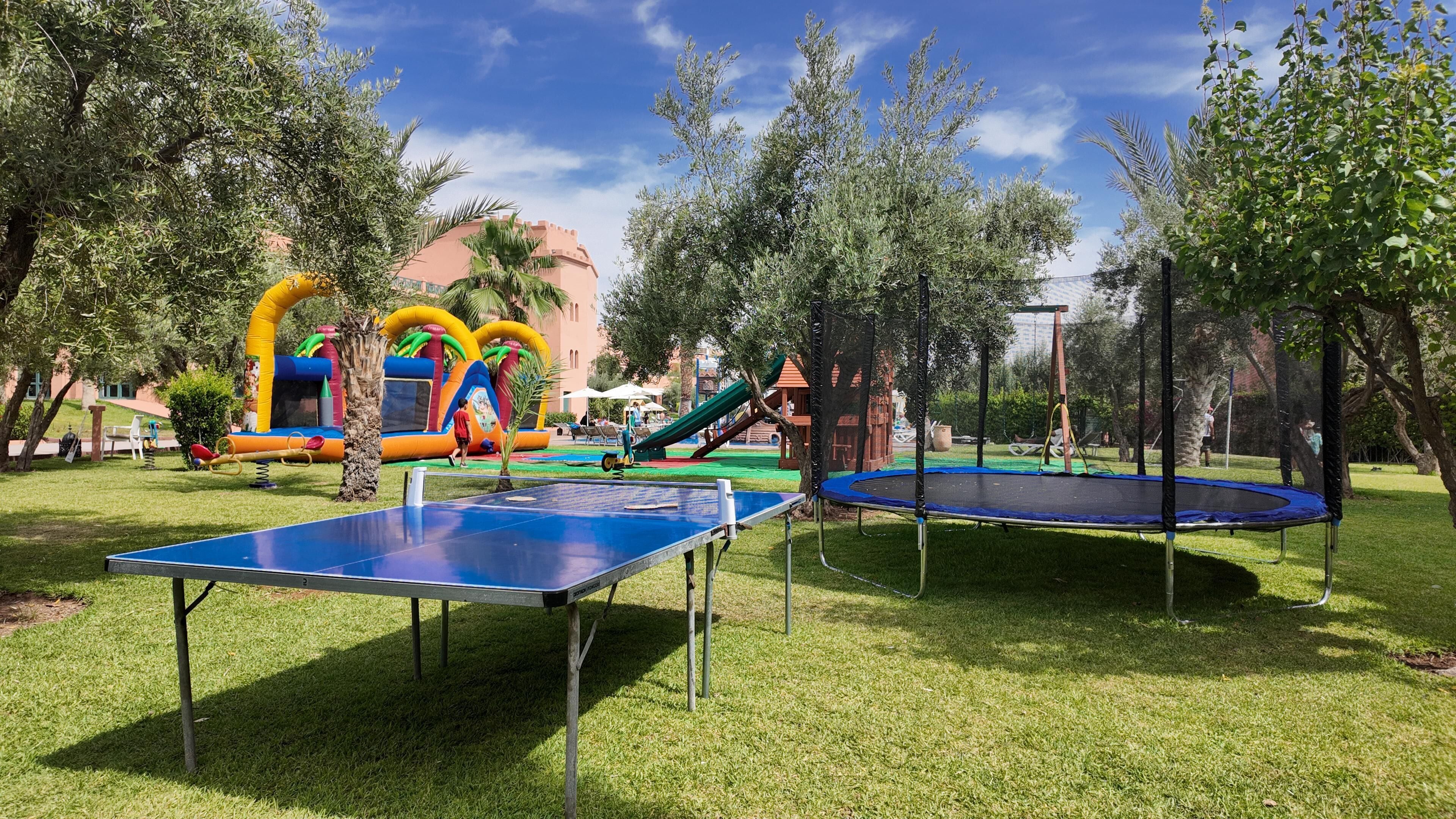 Ein Freizeitbereich im Freien mit einer Tischtennisplatte, einem Trampolin und aufblasbaren Spielgeräten.