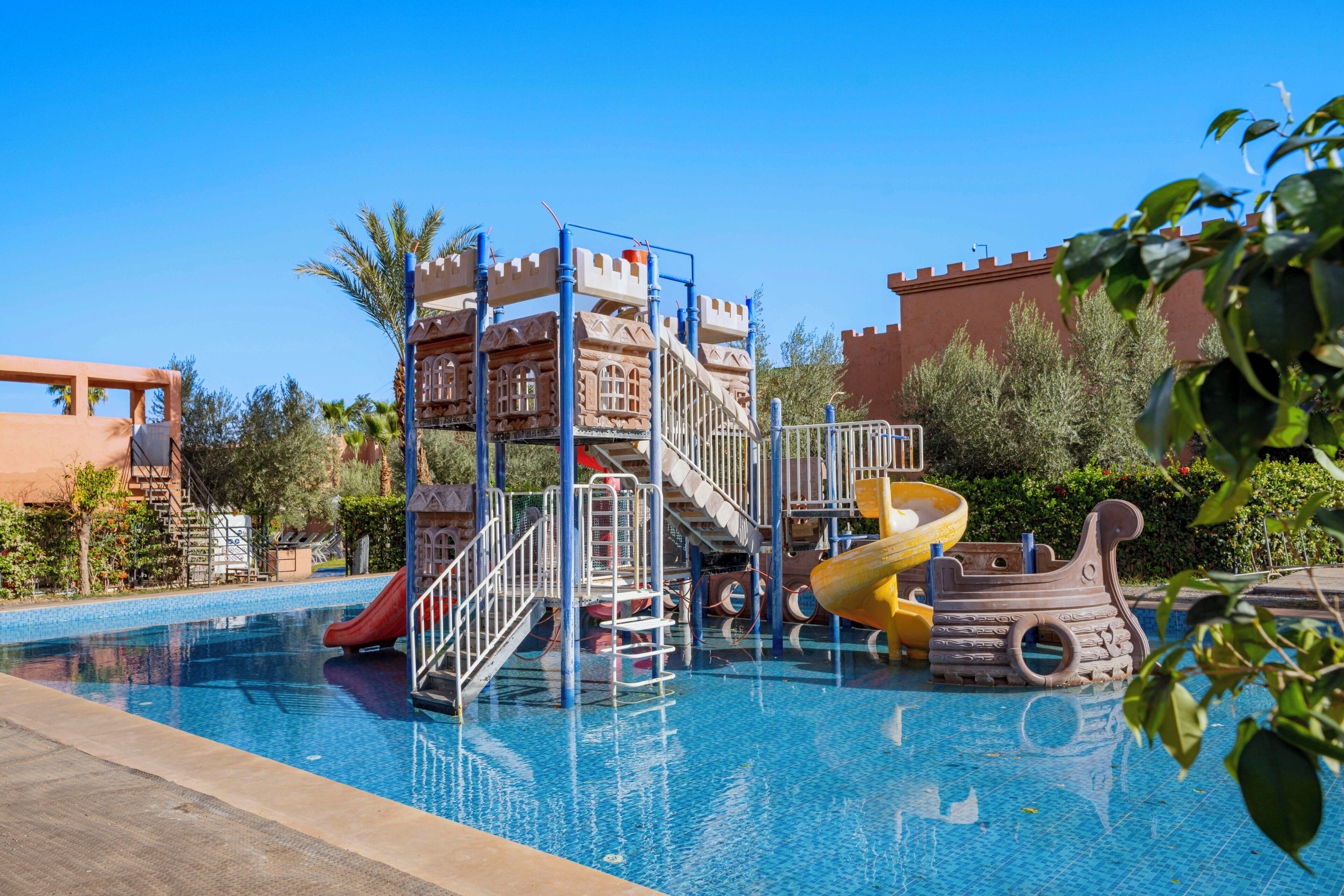 A swimming pool with a castle-themed play area, including slides and a ship-shaped structure.