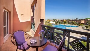 Un balcón con mesa y sillas, con vista a una piscina y edificios de un complejo turístico.