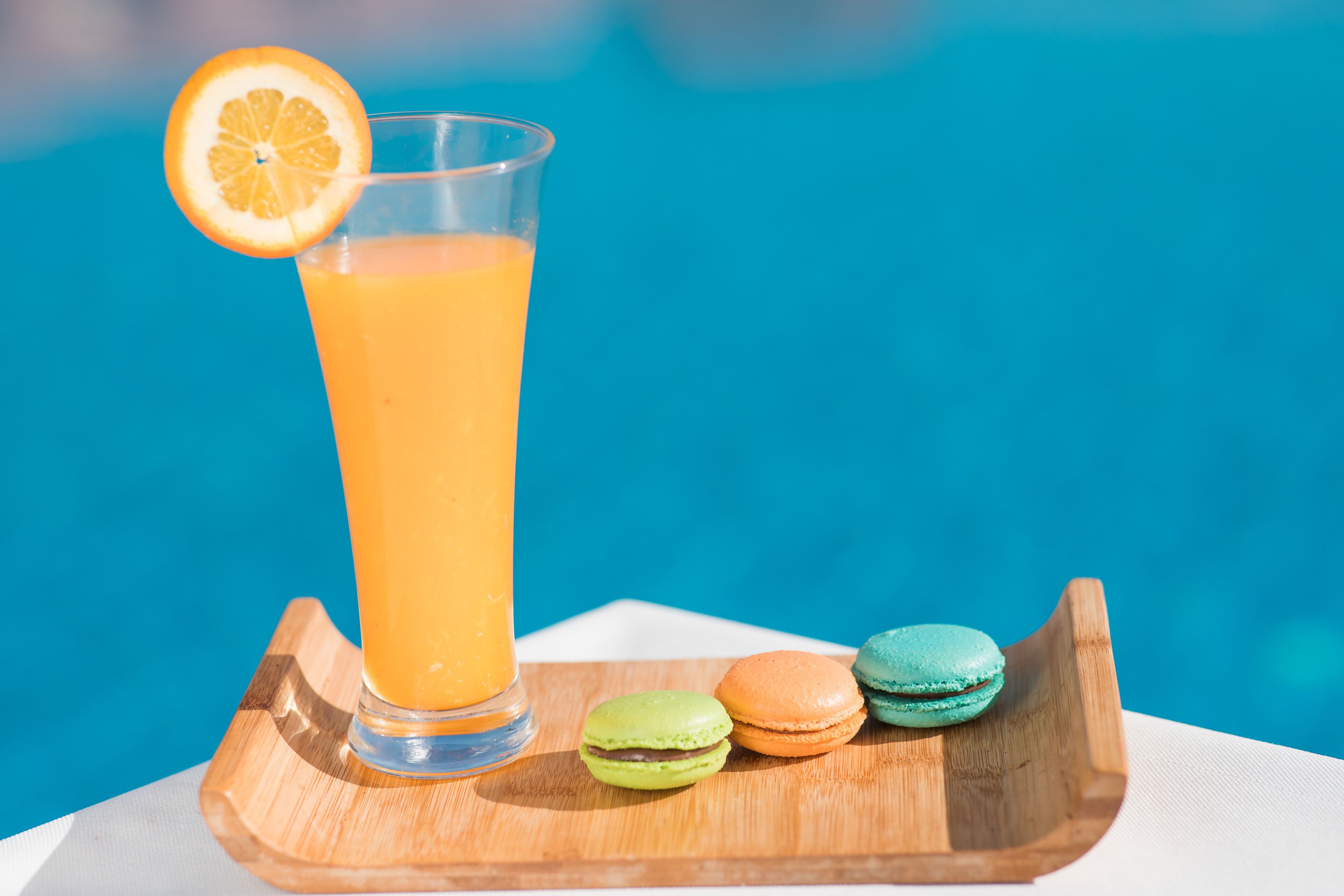 Um copo de suco de laranja com uma fatia de laranja sobre uma bandeja de madeira.