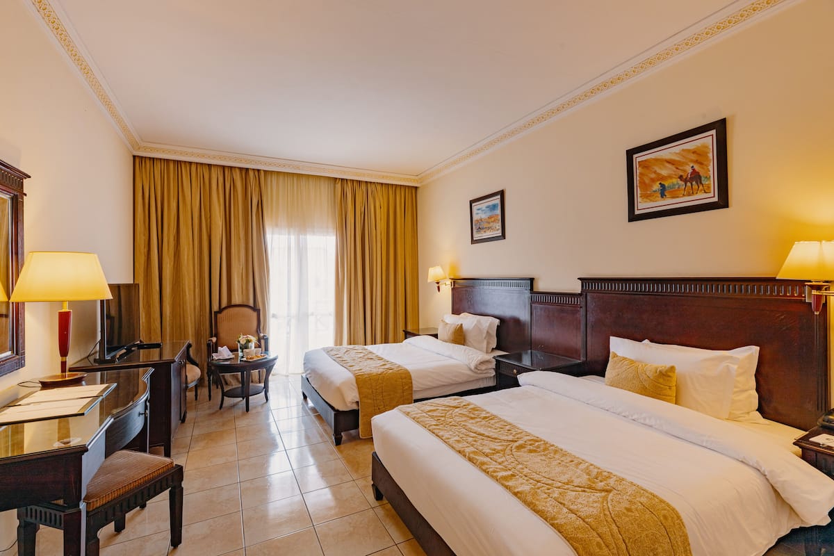 A hotel room with two beds, a desk, a chair, and a window with curtains.