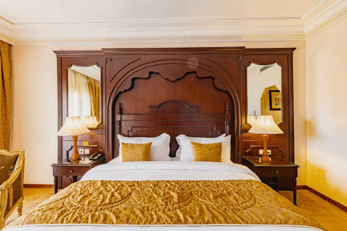 A hotel room with a large bed, wooden headboard, two bedside tables with lamps, and a mirror.