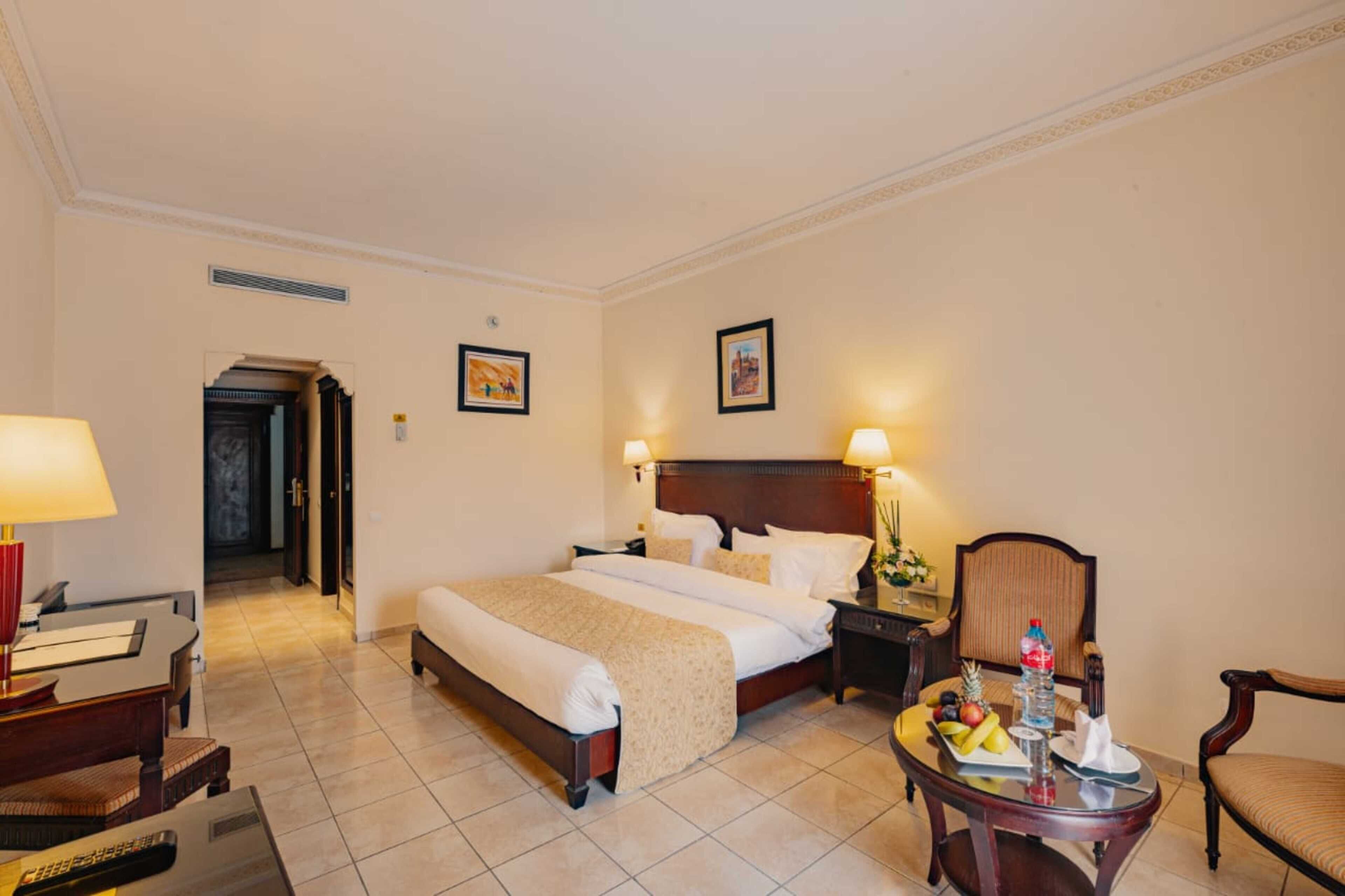 A hotel room with a large bed, bedside tables, a desk with a lamp, and a chair.