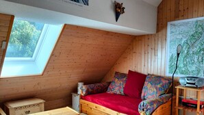 Un acogedor dormitorio tipo loft con techo inclinado de madera, un sofá rojo con cojines de colores, una pequeña mesa de madera, una radio en un estante de madera y un mapa en la pared.
