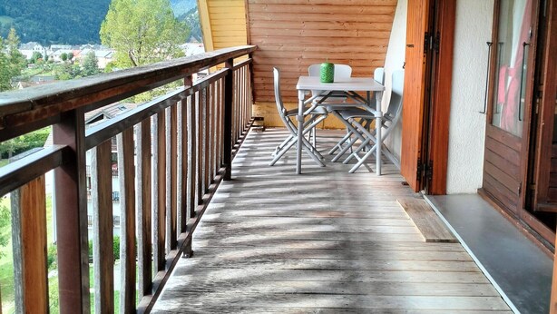 Un balcón de madera con una mesa y sillas, con vistas a un paisaje con casas y colinas.