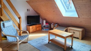 Un cuarto ático acogedor con techo inclinado, muebles de madera, televisor y estantería.