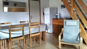 Una cocina compacta con refrigerador, armarios de madera y un comedor con mesa y sillas.