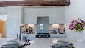 Una cucina moderna con mobili bianchi, un'isola centrale con piano cottura e una trave in legno rustica.