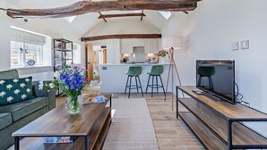 Un soggiorno moderno con travi a vista in legno, una TV, un divano, un tavolino da caffè e una cucina sullo sfondo.