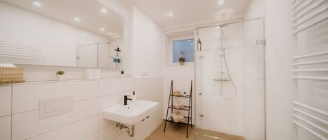 A modern bathroom with a glass-enclosed shower, a white sink, and a small window.