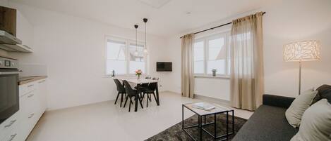 A modern living room with a grey sofa, a coffee table, and a dining area with a table and chairs.