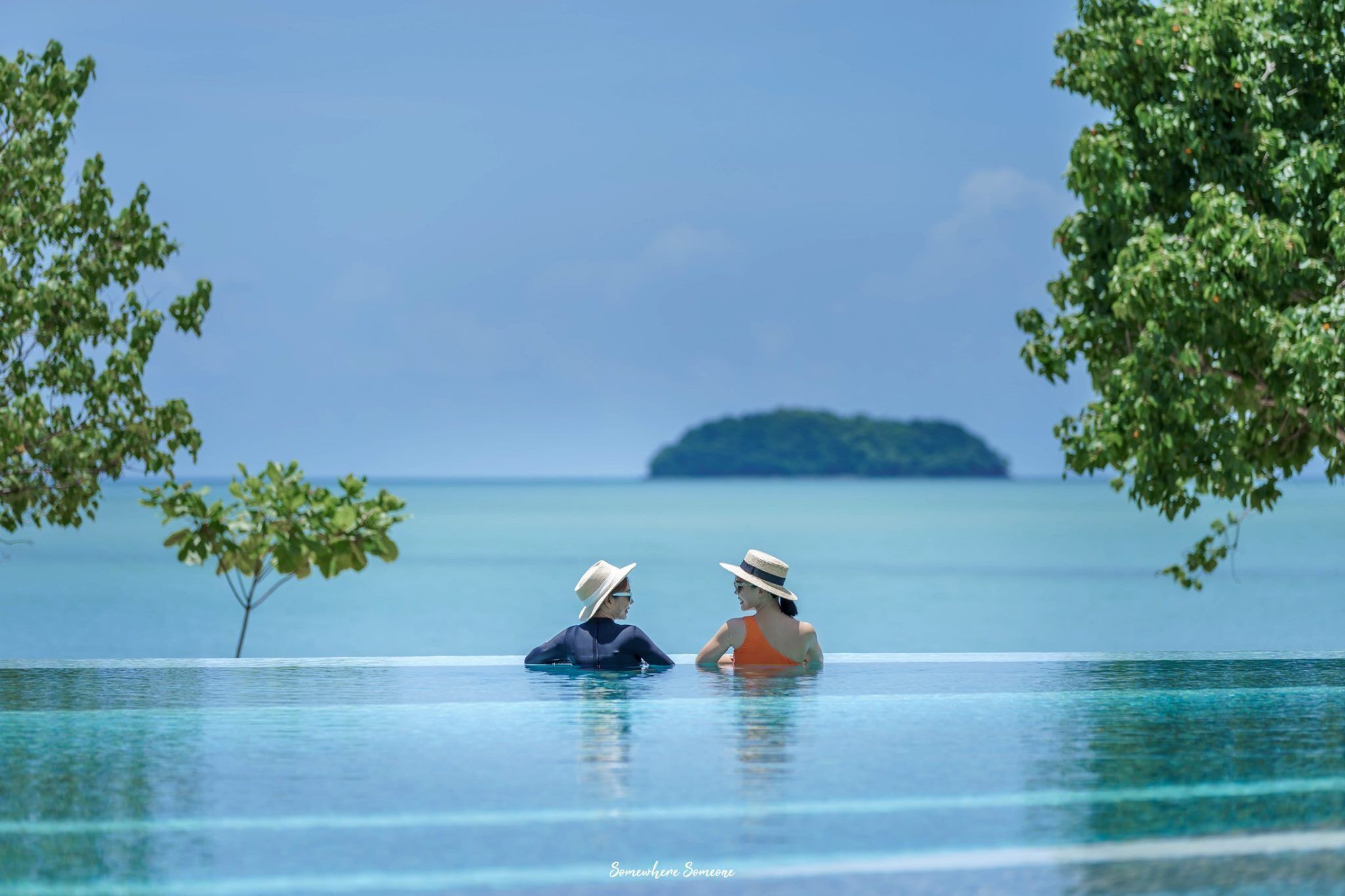 Una pareja en una piscina infinita con vistas al océano y una isla distante.