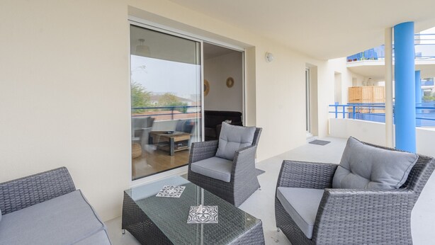 A balcony with wicker furniture, a glass table, and a view of the interior.