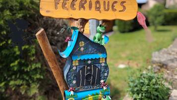 A wooden sign with the text 'LES CABANES FÉRIQUES' and a birdhouse with a frog figure and decorative elements.