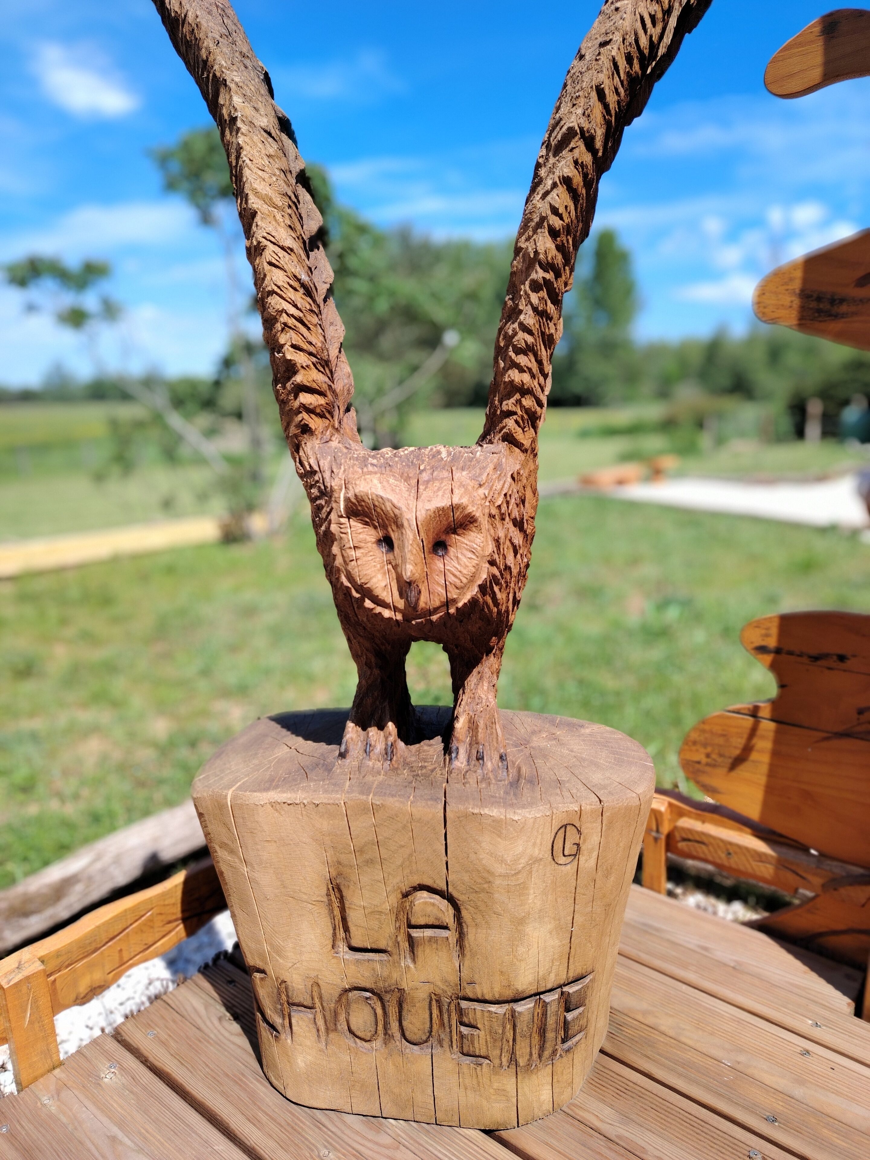 Eine hölzerne Eule Skulptur auf einem Holzfuß, mit der Aufschrift 'LA HOUSETTE'.