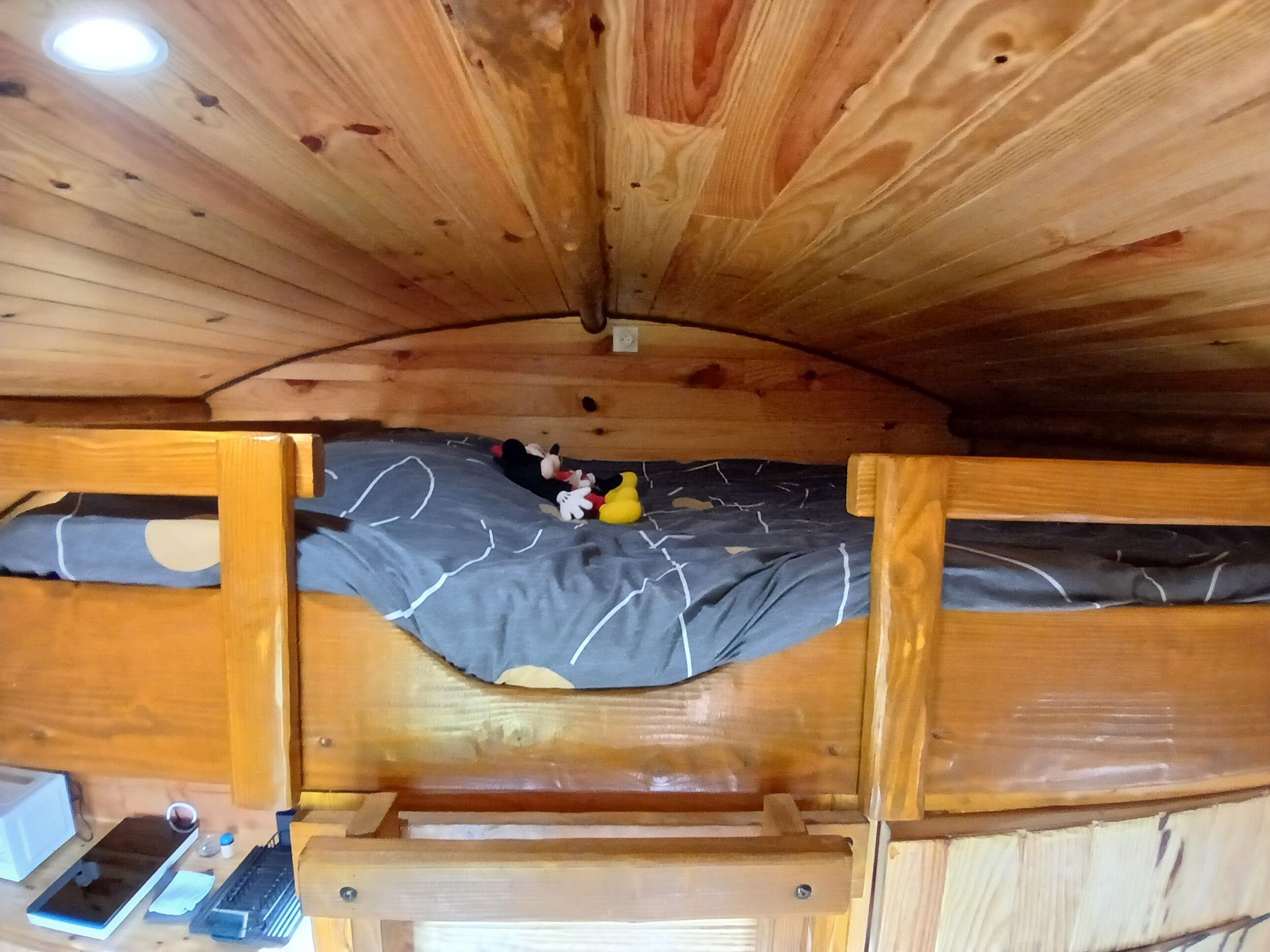 Een houten blokhut binnen met een stapelbed, een bureau met een laptop en een kleine tafel met een fles en een beker.