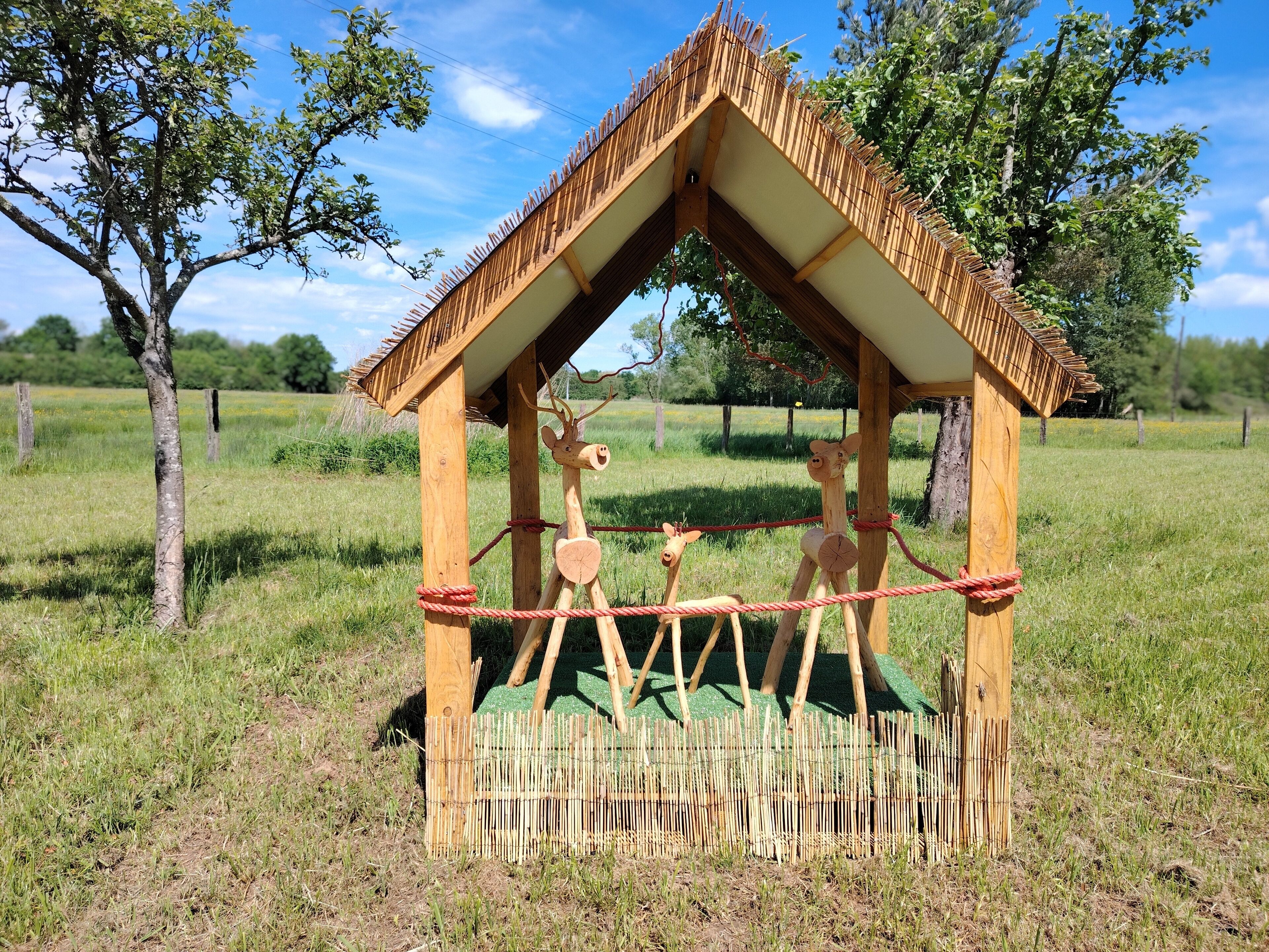 A wooden structure resembling a house with a thatched roof, two wooden giraffe figures, and a rope barrier.