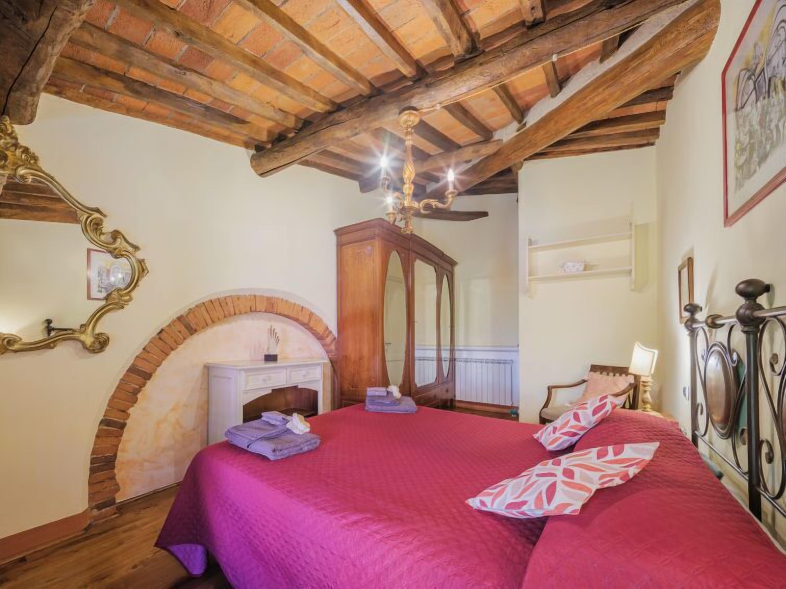 Un dormitorio con techo de madera, chimenea, cama con ropa de cama roja y candelabro.