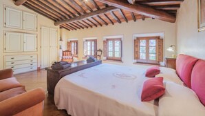 Quarto com cama grande, vigas de madeira, cómoda e uma cadeira.