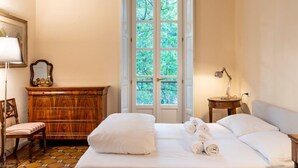 Een netjes ingerichte slaapkamer met een bed, een dressoir, een stoel en een raam met uitzicht op bomen.