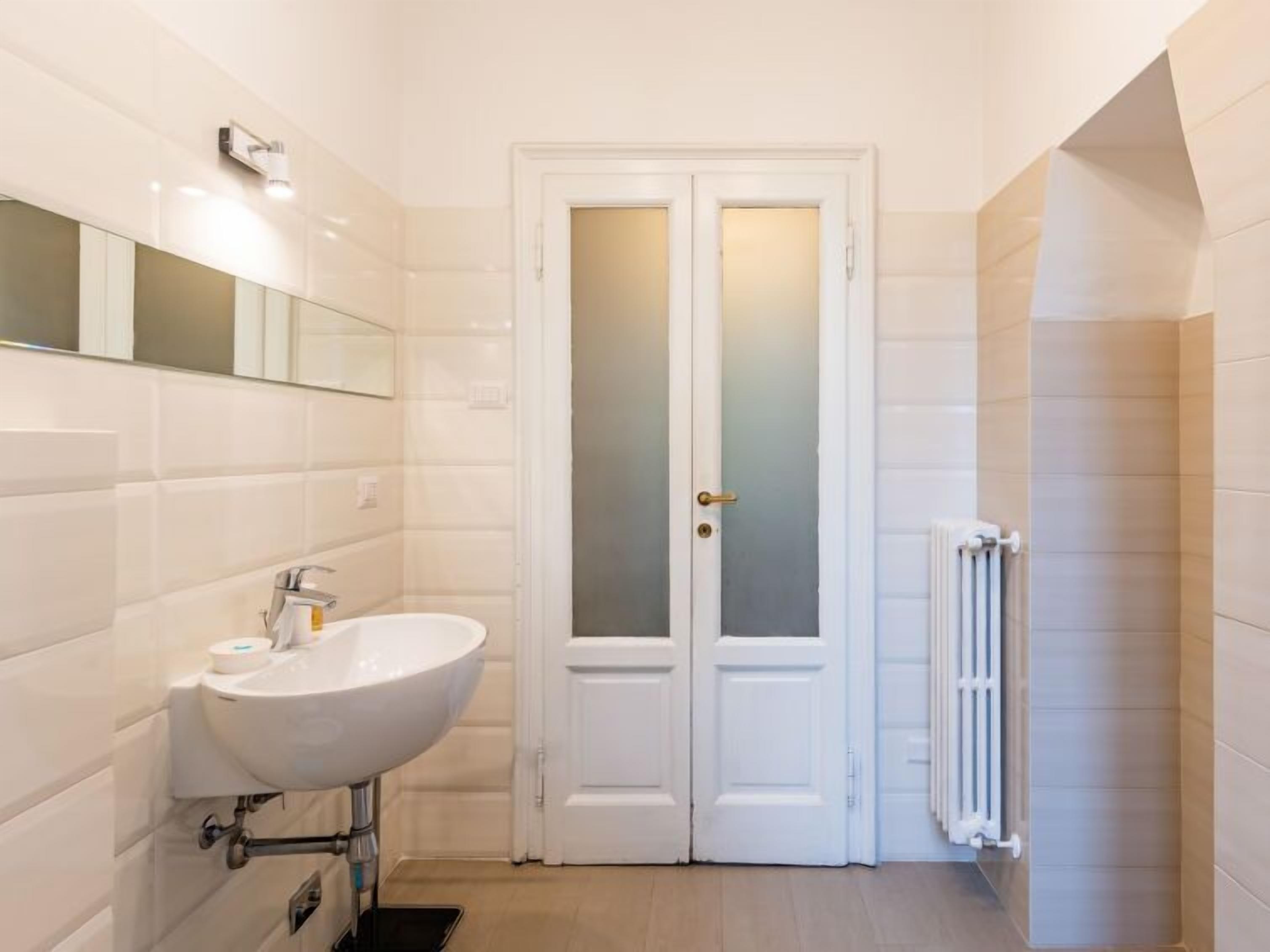 A modern bathroom with a white sink, double doors, and a radiator.