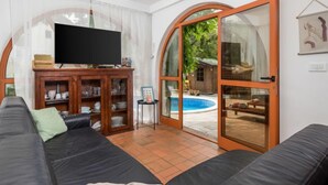 Ein Wohnzimmer mit einem schwarzen Ledersofa, einer Hollauslage mit Glastüren, einem Flachbildfernseher und einer Glastür zu einem Außenbereich mit Pool.