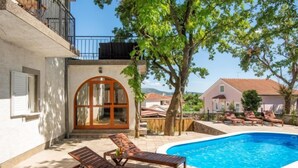 Ein privater Poolbereich mit Liegestühlen, einer Holztür und Blick auf benachbarte Häuser.