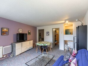 A compact living space with a sofa, a dining table, a TV, and a kitchenette.