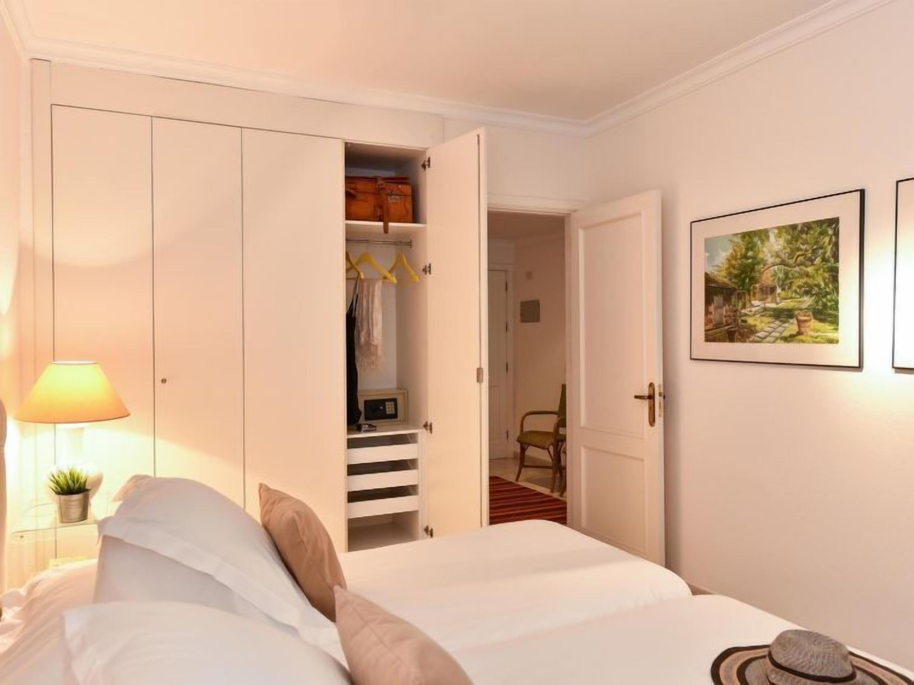 Una camera d'albergo con un letto, un armadio, una lampada e un quadro appeso al muro.