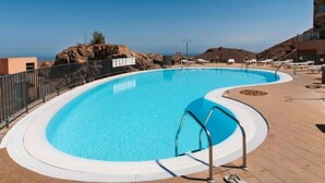 Piscina azul cristalina con una escalera de metal, rodeada por una terraza de madera y una valla metálica.