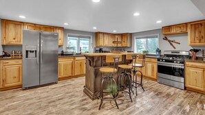 A modern kitchen with wooden cabinets, a stainless steel refrigerator, a central island with bar stools, and a built-in oven.