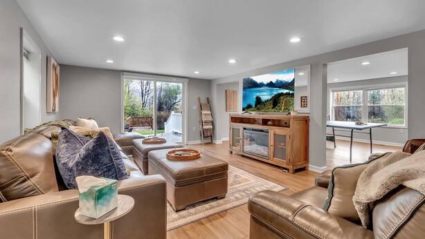 A spacious living room with leather sofas, a wooden cabinet, and a large TV screen displaying a scenic landscape.