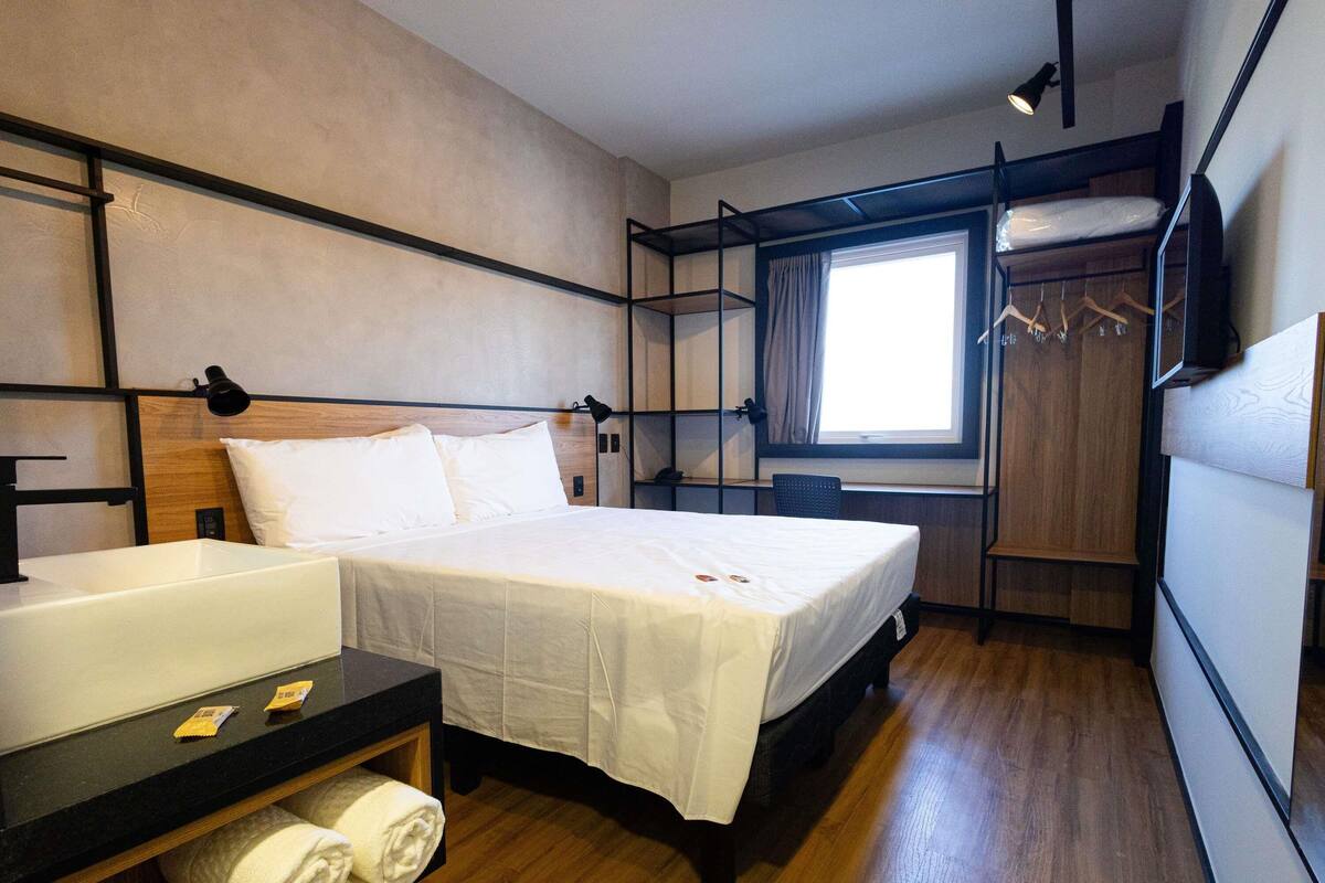 A hotel room with a bed, bedside table, and a window.