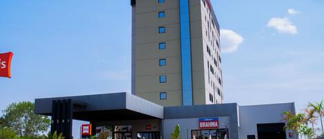 A modern hotel with a prominent 'ibis HOTEL' sign, a 'BRAHMA' restaurant, and a well-maintained entrance area.